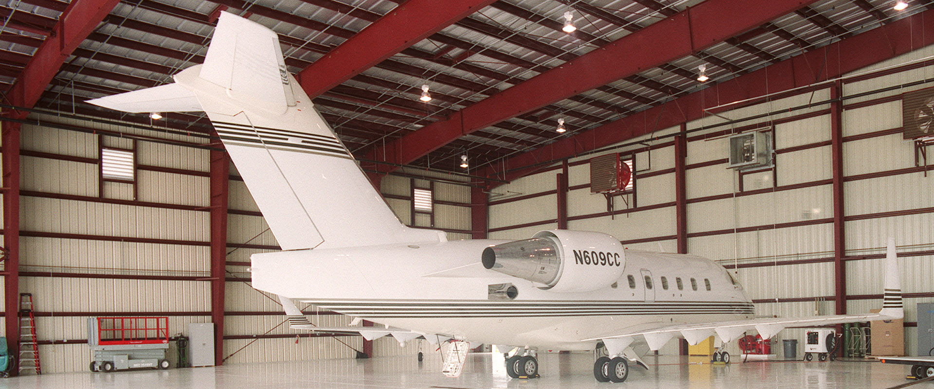 Private jet parked in a spacious aviation hangar with red steel beams and polished flooring, showcasing Leighton McGinn's commitment to quality aviation facilities.