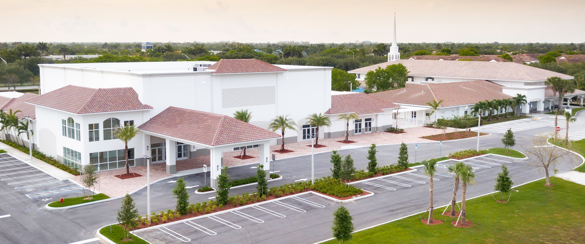 Modern church building with a spacious entrance, palm trees, and a prominent steeple, representing Leighton McGinn's commitment to constructing sacred spaces for faith communities.